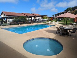 Una piscina con sillas de descanso y sombrillas, rodeada de edificios con tejados rojos.
