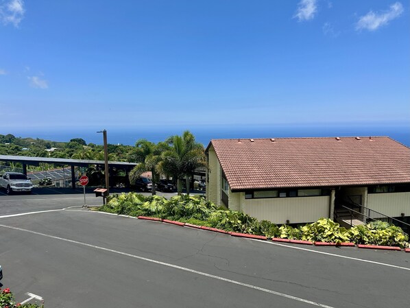 A building with a red-tiled roof, adjacent to a parking lot with a stop sign, and a view of the ocean.