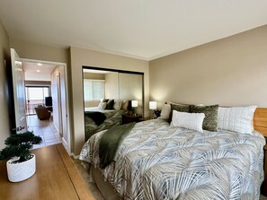 Un dormitorio con una cama grande, una mesita de noche, un espejo y una planta en maceta.