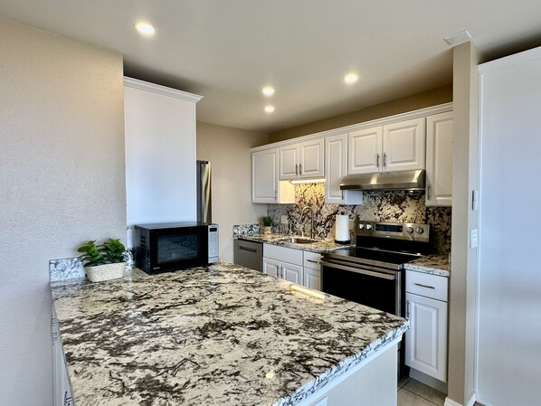 A kitchen with white cabinets, a granite countertop, a microwave, a refrigerator, and a stove.