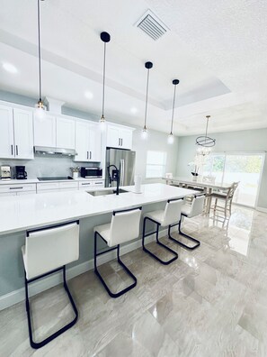 Una cocina moderna con armarios blancos, electrodomésticos de acero inoxidable y una isla grande con taburetes de bar.