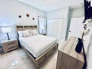 Ein Schlafzimmer mit einem hölzernen Bett, Nachttischen, einem Schreibtisch und einer Topfpflanze.