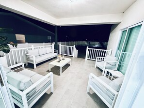 Ein zeitgemäßer Außenbereich zum Verweilen mit weißer Möbel, darunter Sofas, Sessel, ein Couchtisch und einer Geländer.
