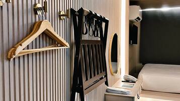 A hotel room with a bed, a bedside table, a hanging coat rack, and a mirror.