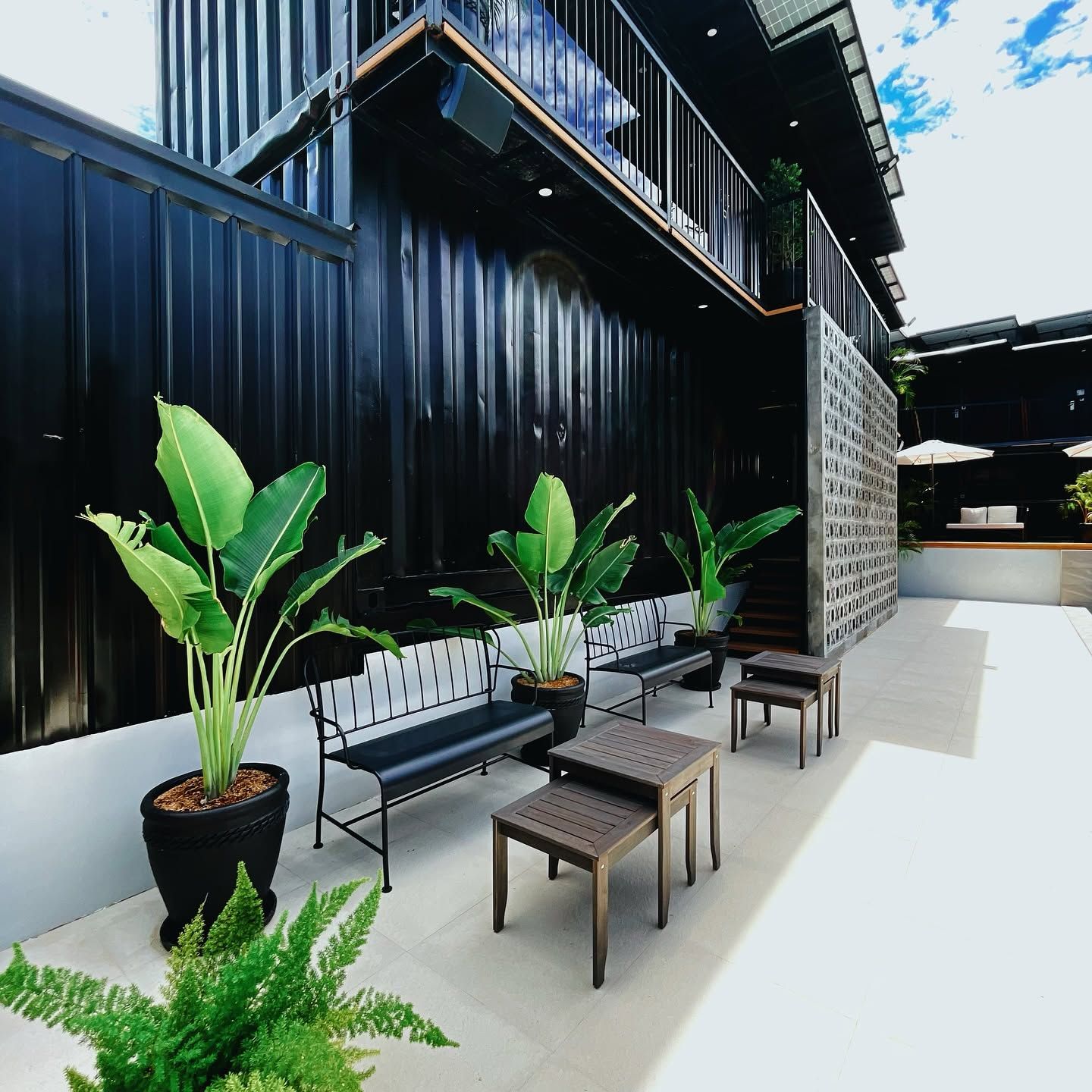 An outdoor seating area with benches and tables, surrounded by potted plants.