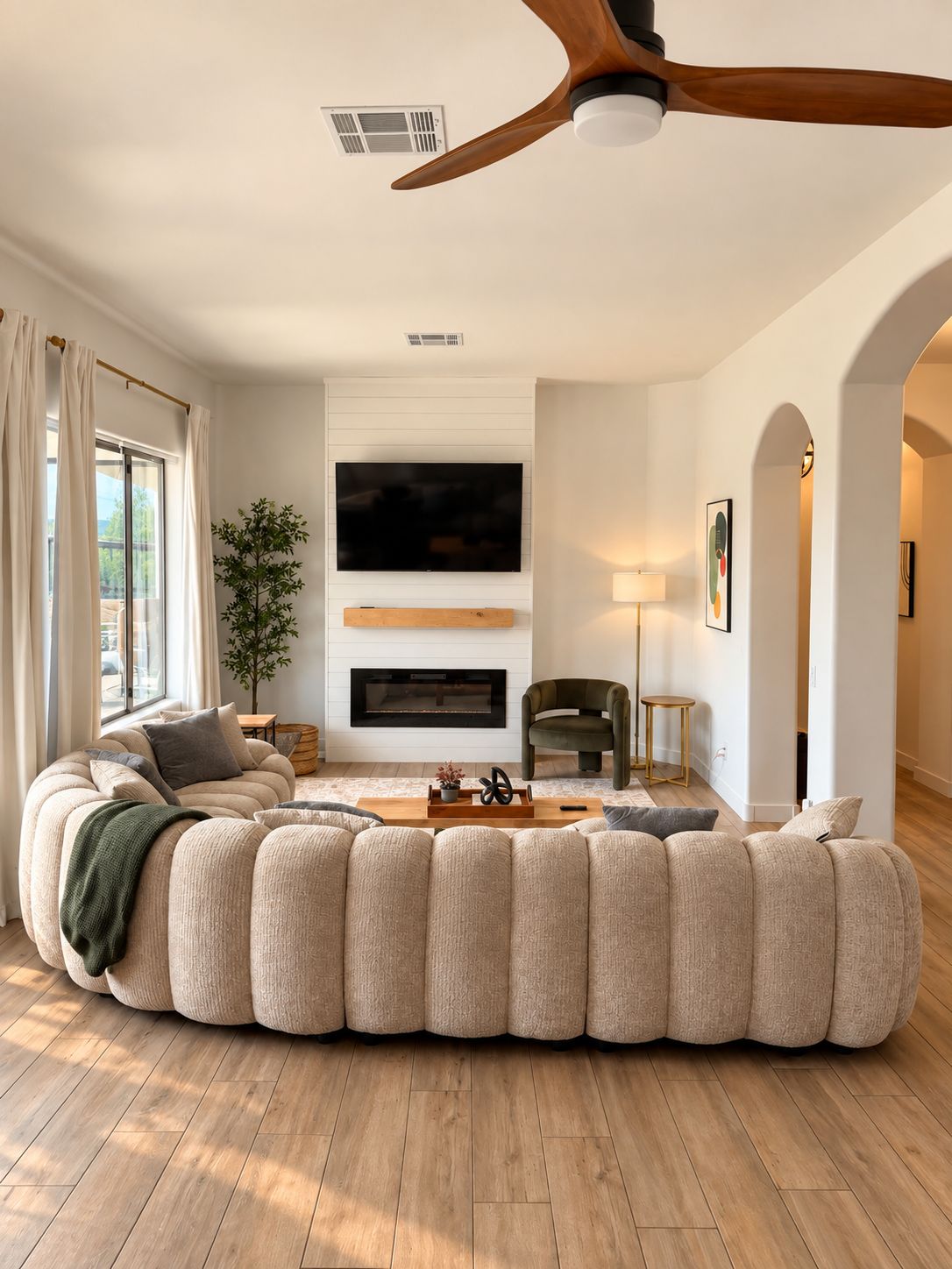 A modern living room with a sectional sofa, a flat-screen TV, a fireplace, and a ceiling fan.