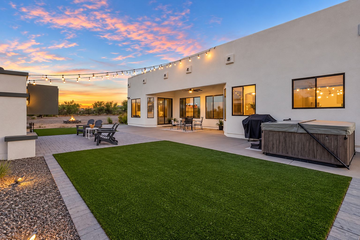 A modern outdoor patio with a barbecue, seating area, and string lights.