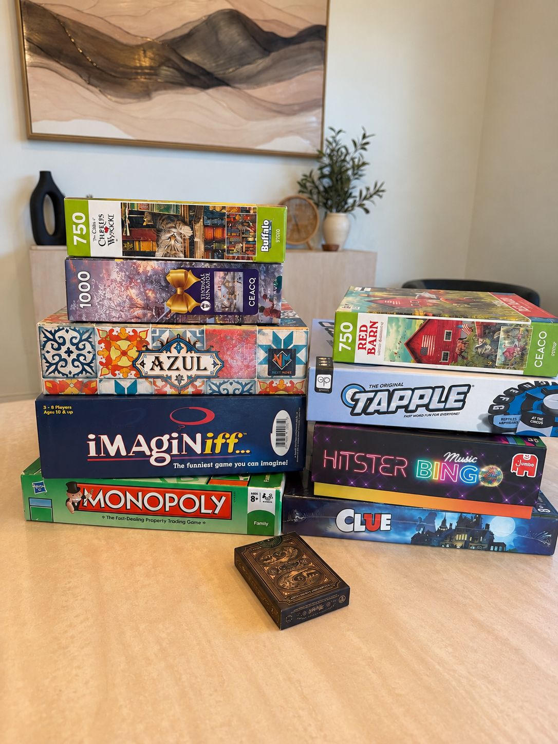 A variety of board games stacked on a table, including 'Azul', 'Monopoly', and 'Clue'.