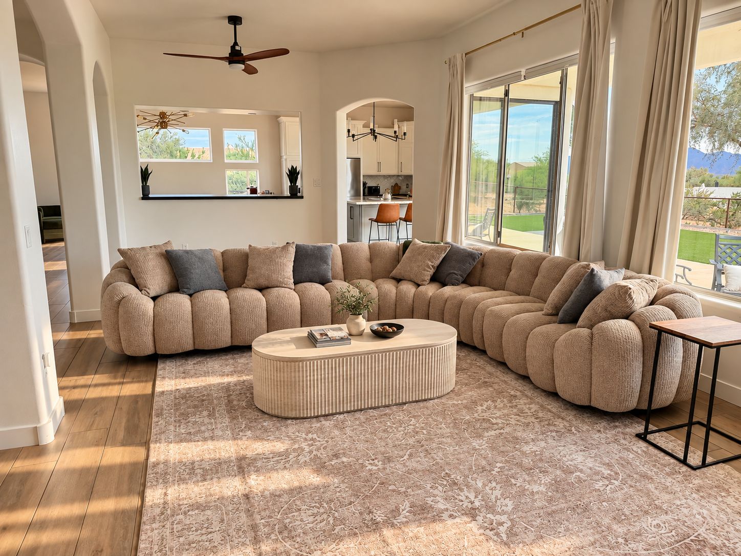 A spacious living room with a large sectional sofa, a round coffee table, and a view of the outdoors through large windows.