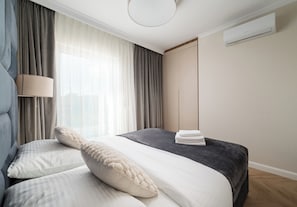 A modern bedroom with a bed, curtains, a lamp, and an air conditioning unit. - Lotnisko Chopina Luxury Apartment (Warszawa)