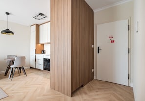 A modern kitchen with wooden cabinets, a built-in oven, and a dining area with a table and chairs. - Lotnisko Chopina Luxury Apartment (Warszawa)