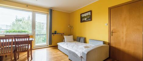 Una habitación con una cama, una mesa de comedor con sillas, un cuadro en la pared y una puerta.