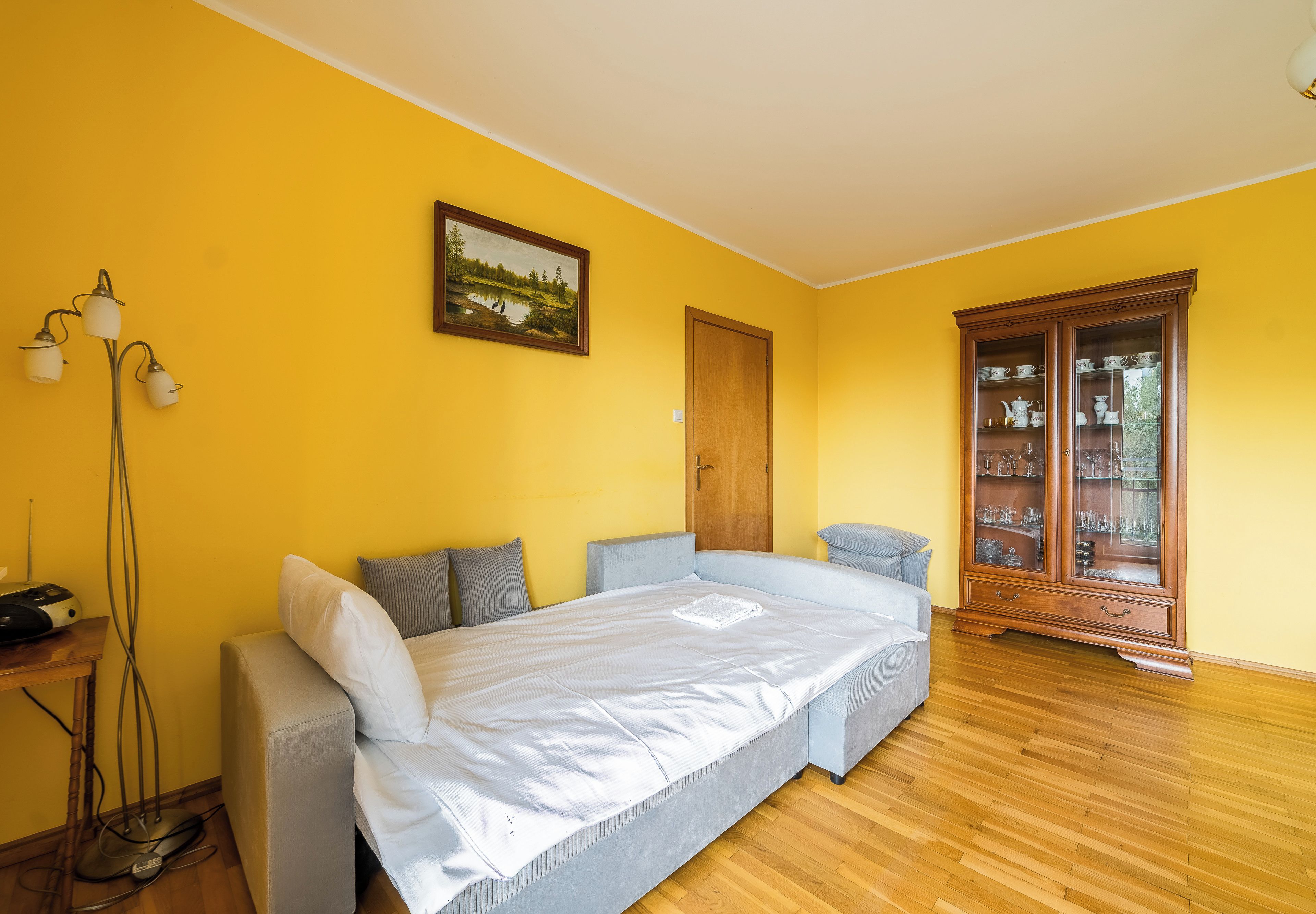 A bedroom with a bed, bedside table, lamp, and a cabinet with glass doors.
