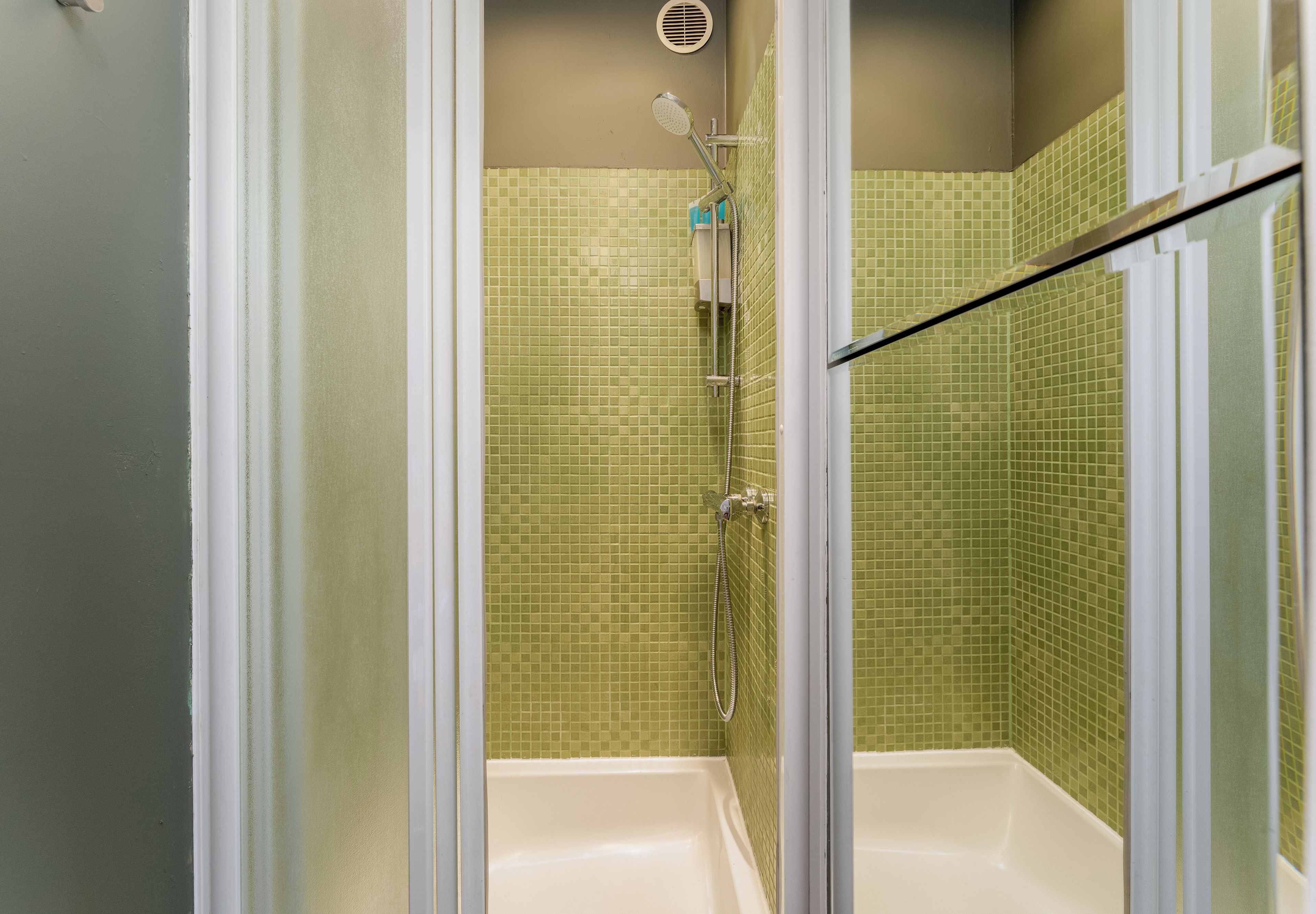 Une douche avec une porte en verre, une douchette à main et un panneau de commande fixé au mur.