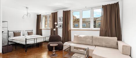Et moderne soveværelse med seng, sofa, stol, lille bord og et vindue med gardiner.