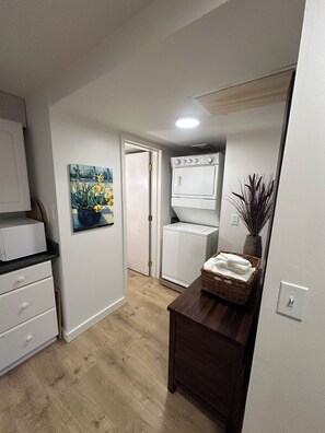 A compact kitchen with white cabinets, a white oven, and a wooden dining table with a basket of towels.