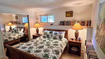 Un dormitorio con una cama de madera, dos lámparas de noche, una ventana, una estantería y un espejo.