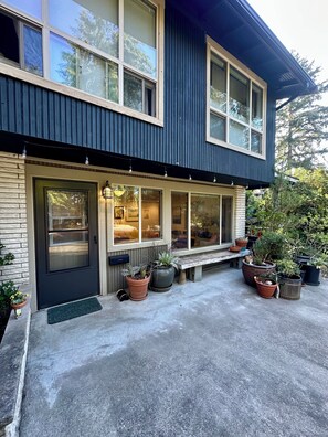 A two-story house with a dark exterior, large windows, and a front porch with potted plants.