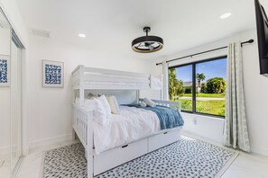 Ein Schlafzimmer mit Etagenbett, Deckenventilator, großem Fenster und Blick auf Grünflächen sowie einem gemusterten Teppich.