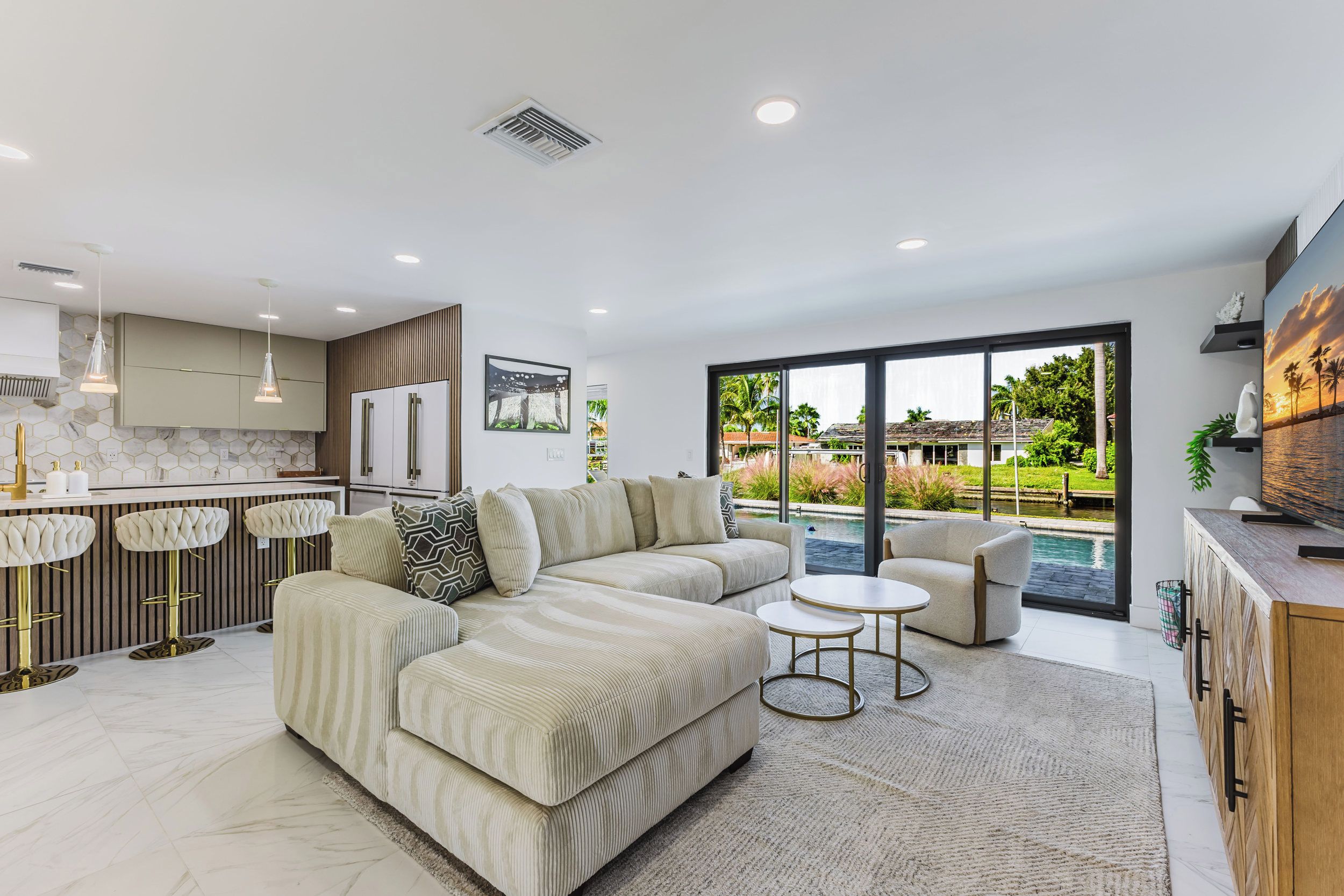 A modern living room with a sectional sofa, a small round table, and a view of a swimming pool through large windows.