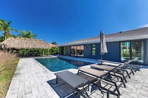 A modern pool area with lounge chairs and a thatched structure. - Welcome to Triton Tiki! W/heated Pool, Located in Cape Coral’s premier 33904 (Cape Coral)