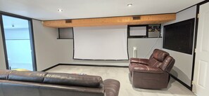 Une salle de cinéma maison équipée d’un grand écran, d’un fauteuil inclinable en cuir et d’un canapé.