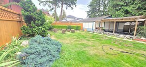 Un jardin avec une terrasse en bois, un mur en pierre et un espace patio couvert.