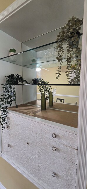 A bathroom with a glass shower enclosure, a white vanity with decorative paneling, and a mirror reflecting a plant and a bench. - 70s Home Retreat | Pond, Patio & Movie Lounges (Surrey)