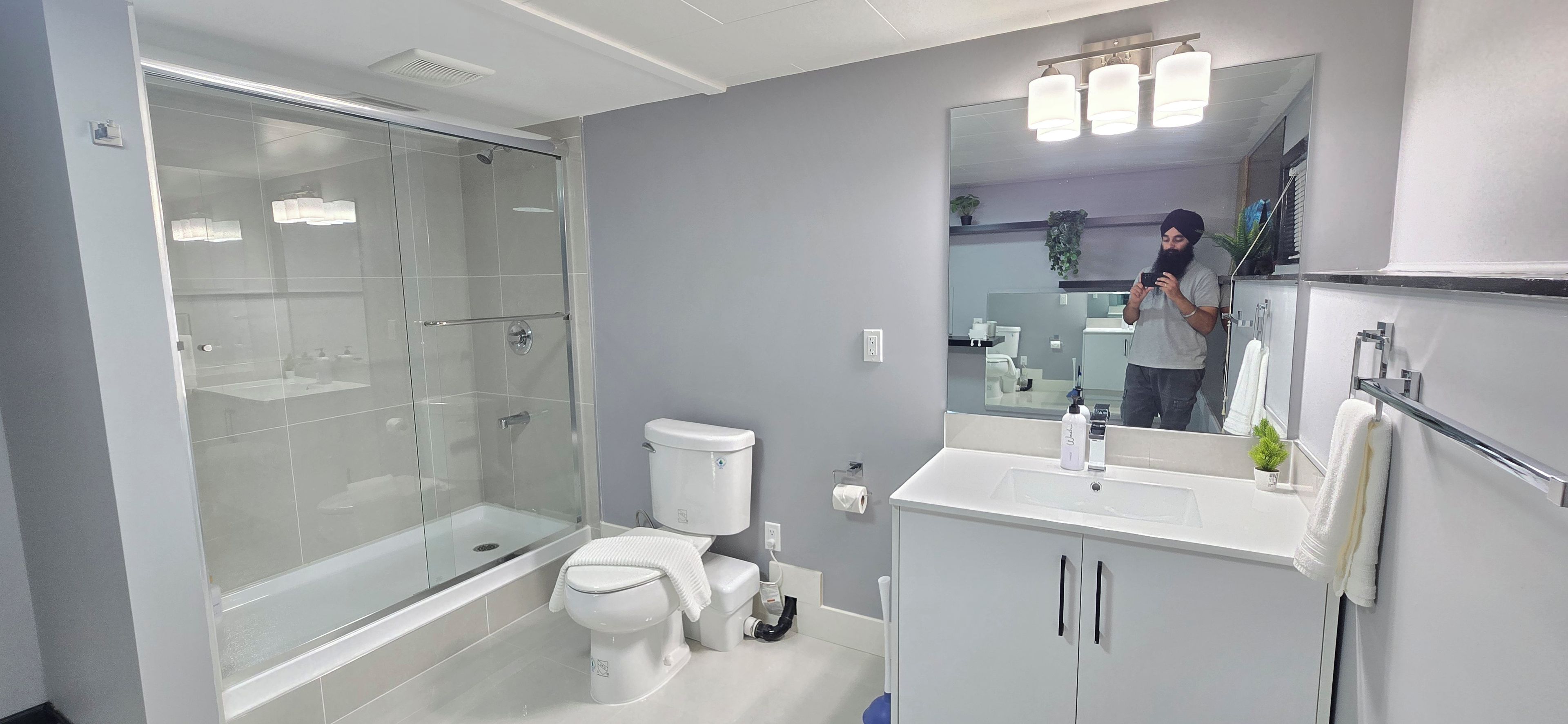 Ein modernes Badezimmer mit einer gläsernen Duschkabine, einer Toilette, einem Waschbecken mit Spiegel und einem Schrank.