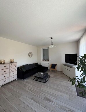 Un salon moderne avec un canapé d’angle, une table basse, un téléviseur et une plante.