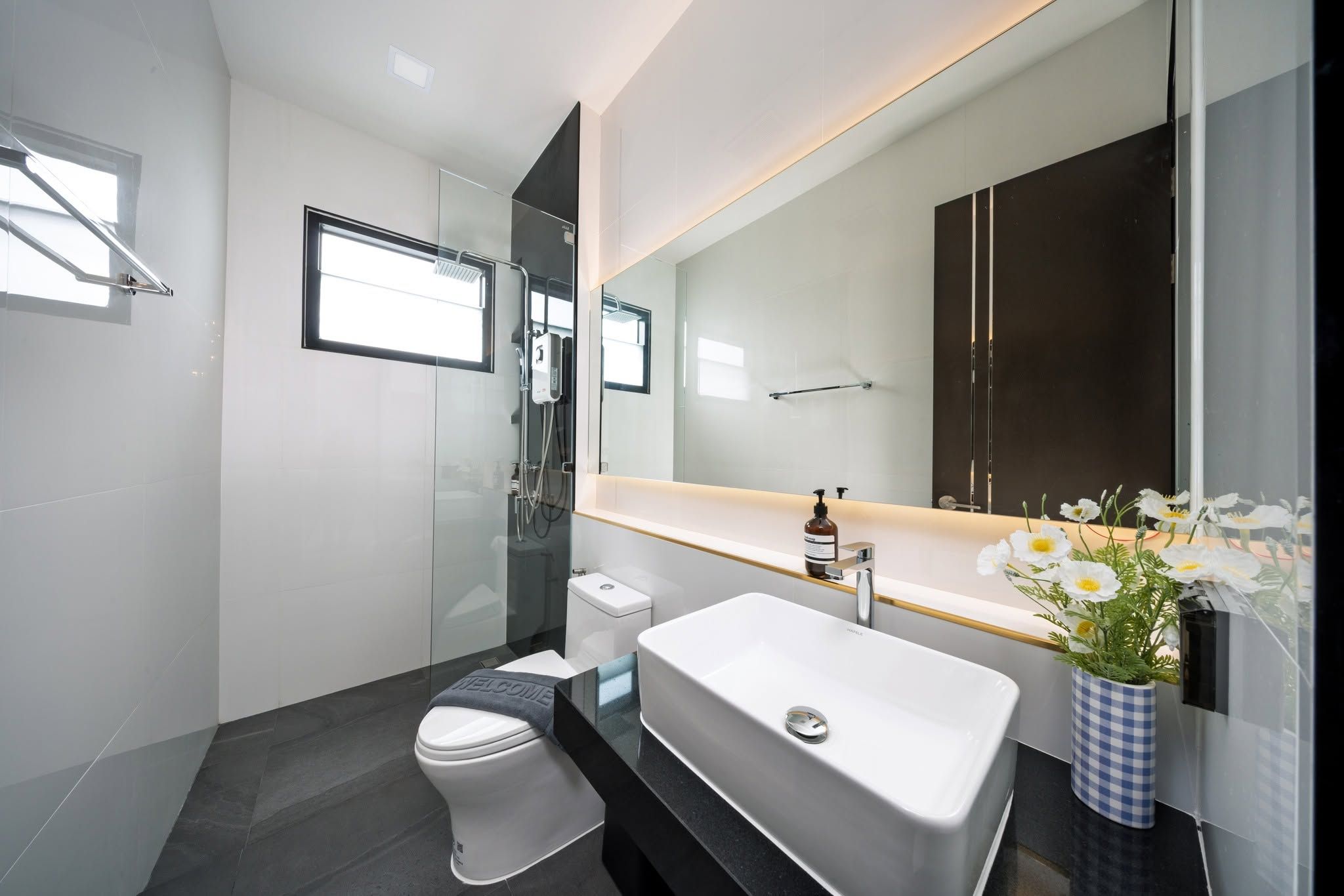 Un baño moderno con un lavamanos blanco, un inodoro, un box de ducha y un espejo grande.