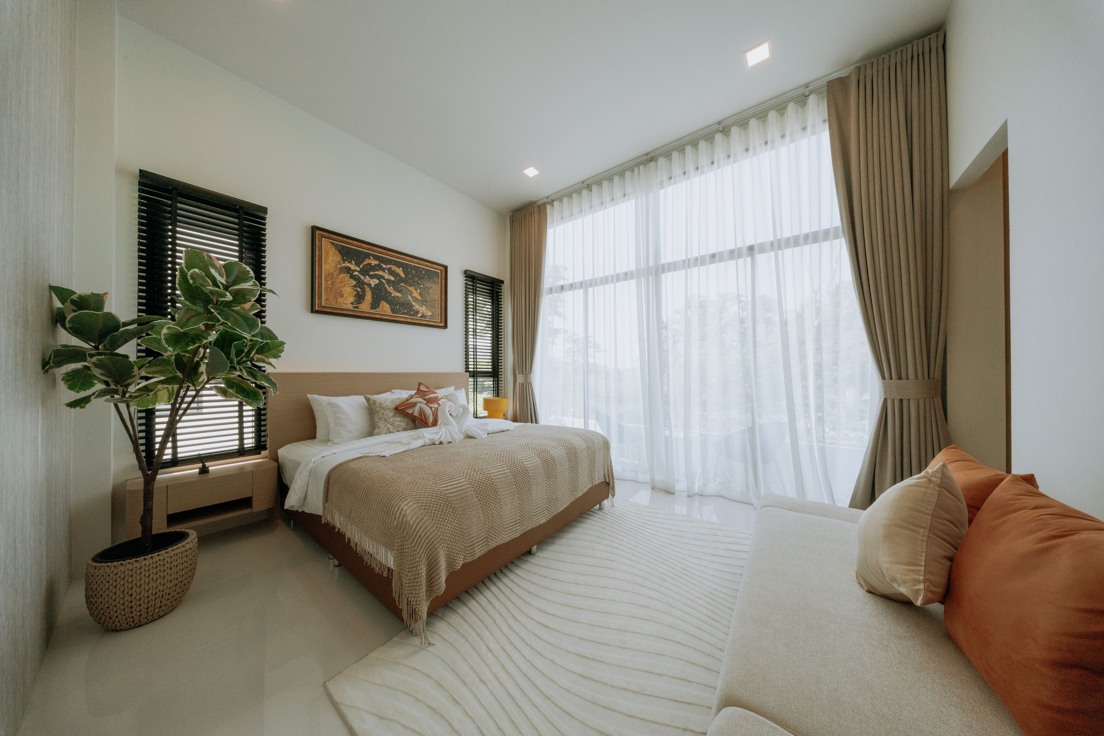 A bedroom with a bed, a sofa, a potted plant, and a painting on the wall.