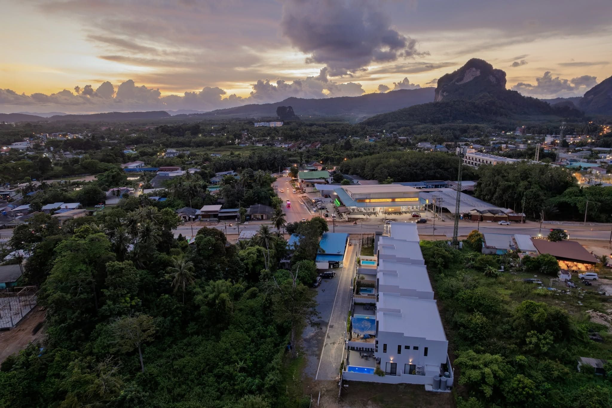 Oversigtsbillede af en by med en markant bygning med fladt tag og swimmingpool, omgivet af grønt og en vej.