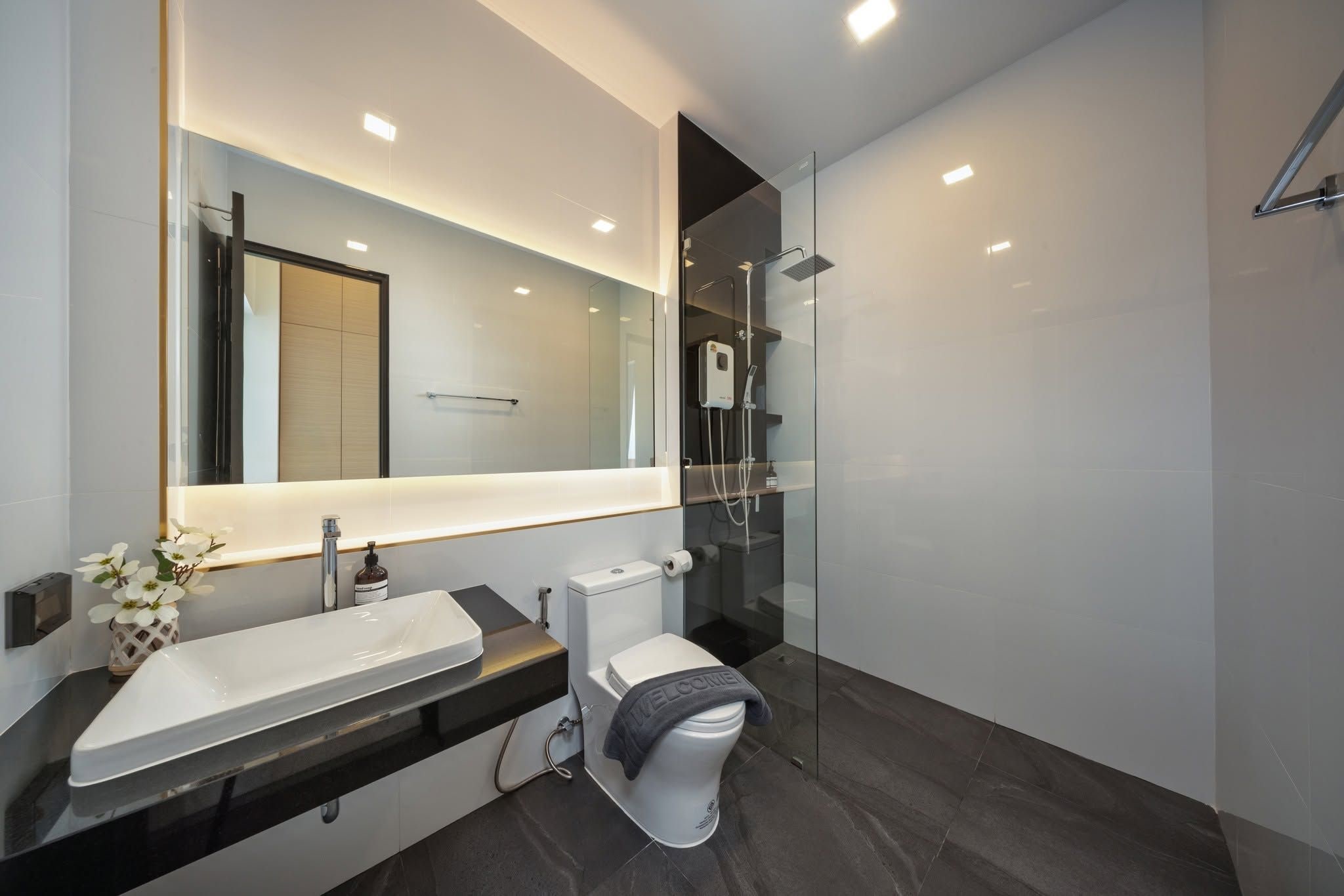 Un baño moderno con un espejo grande, un lavamanos blanco, un inodoro y una cabina de ducha de vidrio.