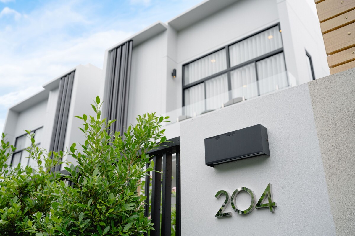 Un edificio moderno con un letrero con el número '204' en la fachada, un buzón negro y una pared de listones de madera a la derecha.