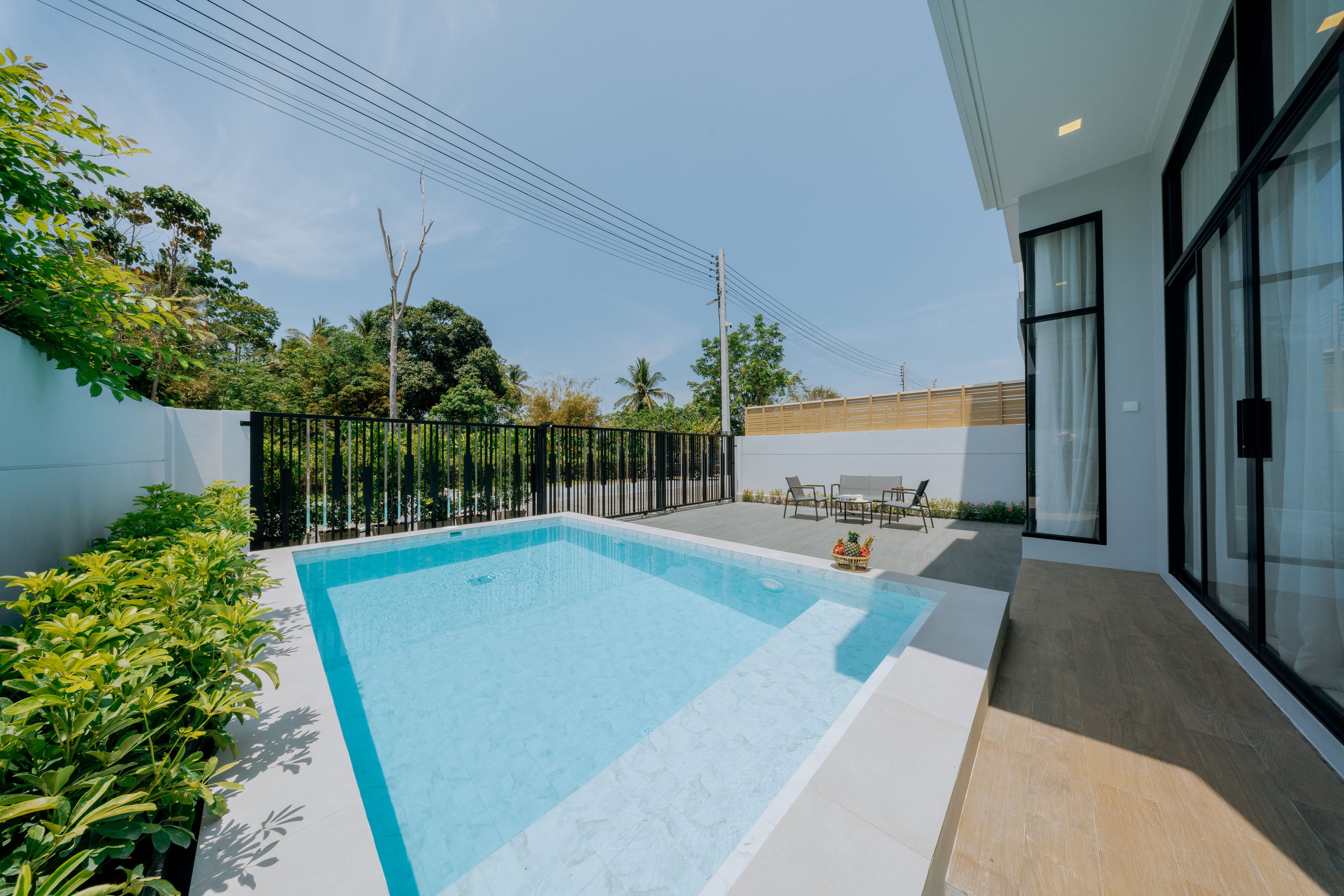 Un área de piscina moderna al aire libre con una piscina azul cristalina, rodeada por una valla baja, y contigua a un edificio con amplias ventanas.