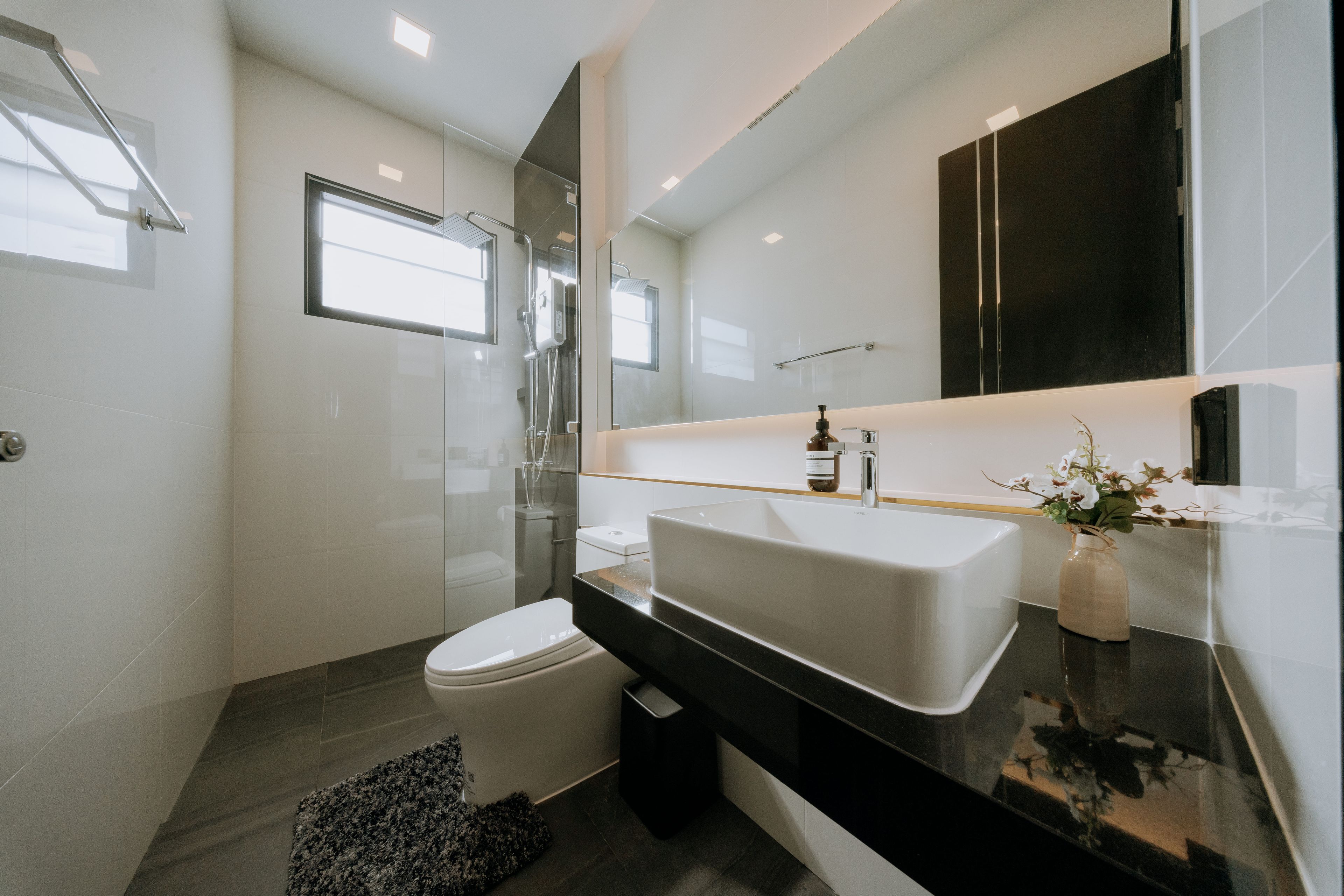 A modern bathroom with a glass-enclosed shower, a white sink, and a black countertop.