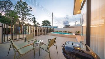 An outdoor patio with a pool, seating area, and a grill.