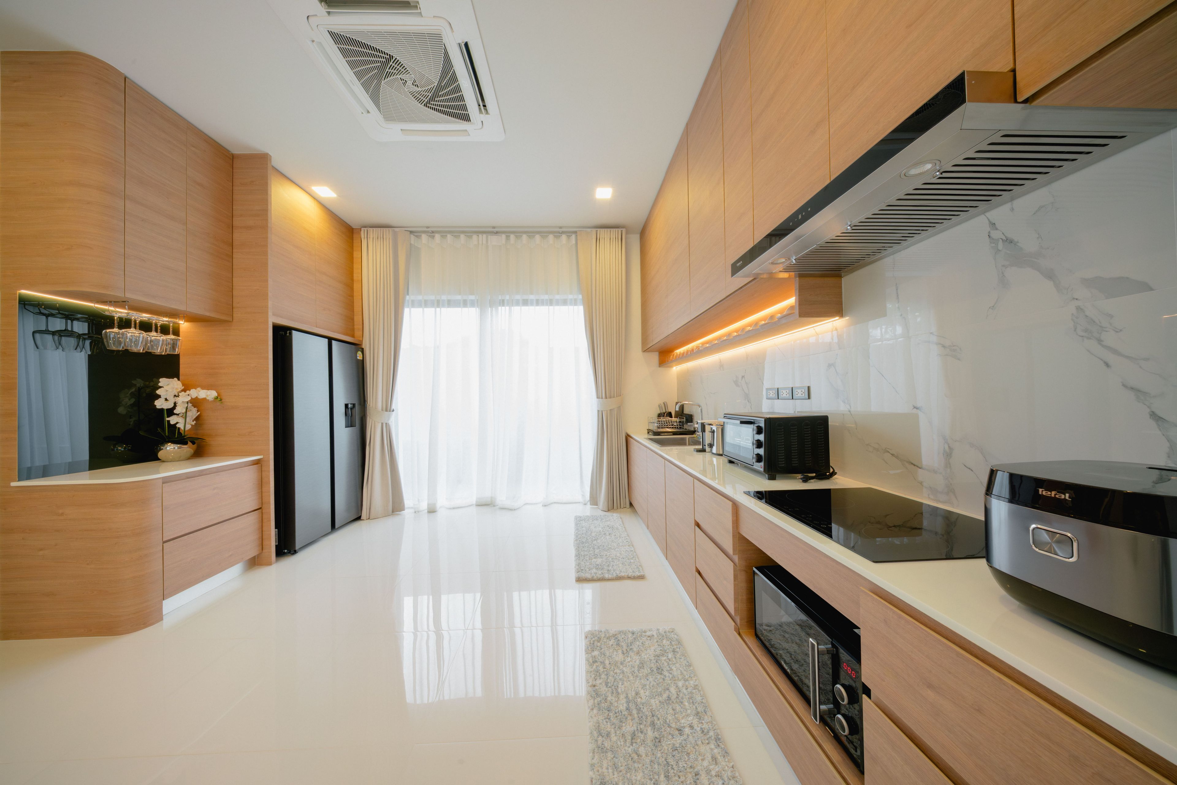 A modern kitchen with built-in appliances, a marble backsplash, and a large window with sheer curtains.