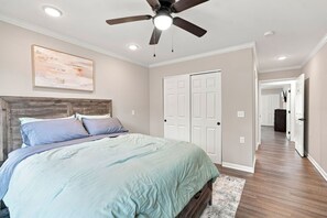 A bedroom with a bed, a ceiling fan, a painting, and a hallway leading to another room. - Spacious Modern 4BR/4BA First-Floor Accessible (Eggertsville)