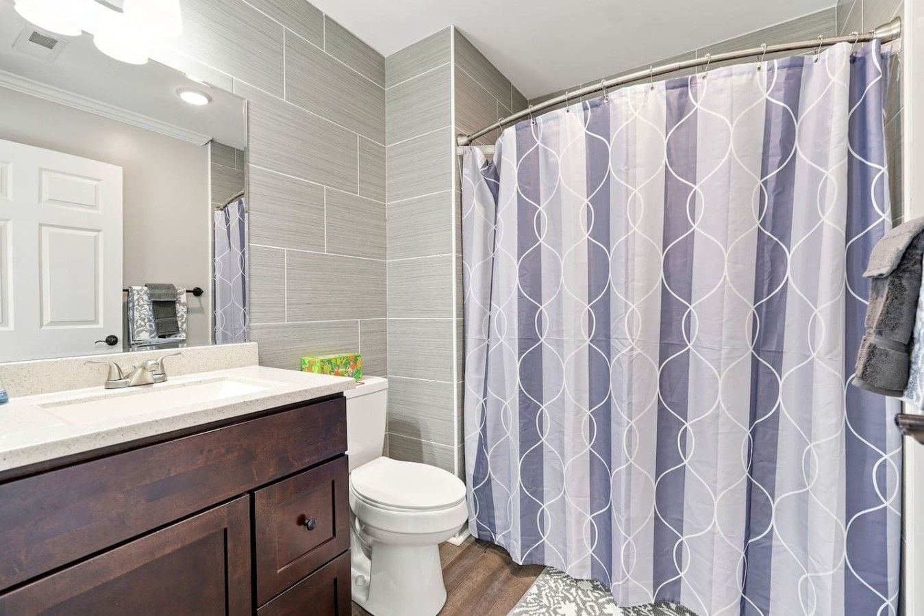 A bathroom with a shower curtain, a toilet, and a vanity with a mirror.