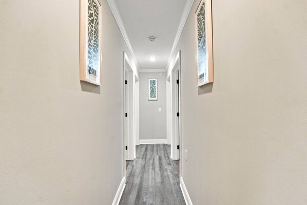 A hallway with a grey carpet, white walls, and a door at the end.