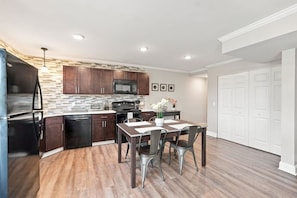 A modern kitchen with dark wood cabinets, a stainless steel refrigerator, and a dining area with a table and chairs.