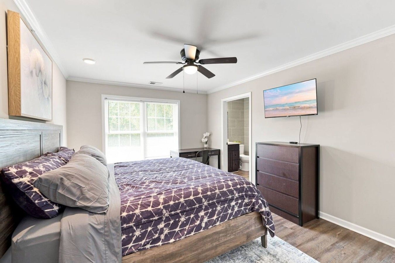 A bedroom with a bed, a ceiling fan, a TV, and a window.