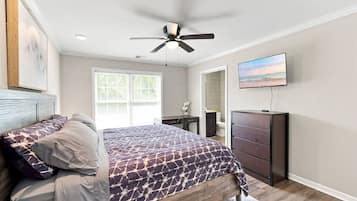A bedroom with a bed, a ceiling fan, a TV, and a window.
