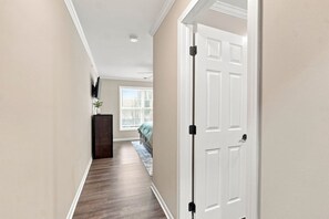 A hallway with a wooden floor, a white door, and a window with blinds.