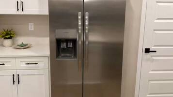 Een koelkast van roestvrij staal met een waterdispenser, witte kasten en een houten vloer.