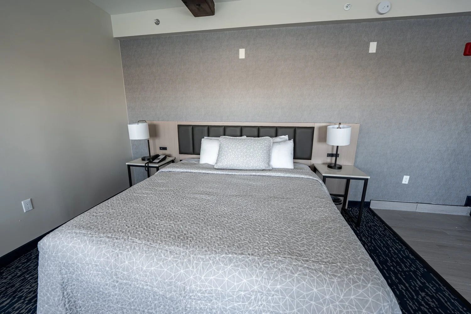 Une chambre d’hôtel avec un grand lit, deux tables de chevet, une tête de lit et un sol recouvert de moquette.
