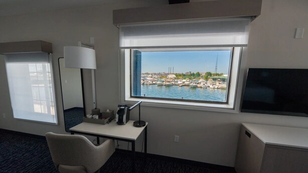 Habitación de hotel con escritorio, silla, televisor y ventana con vista al puerto deportivo.