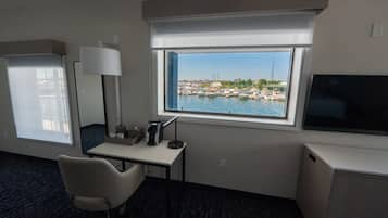 Quarto de hotel com escrivaninha, cadeira, televisão e janela com vista para um areal marítimo.